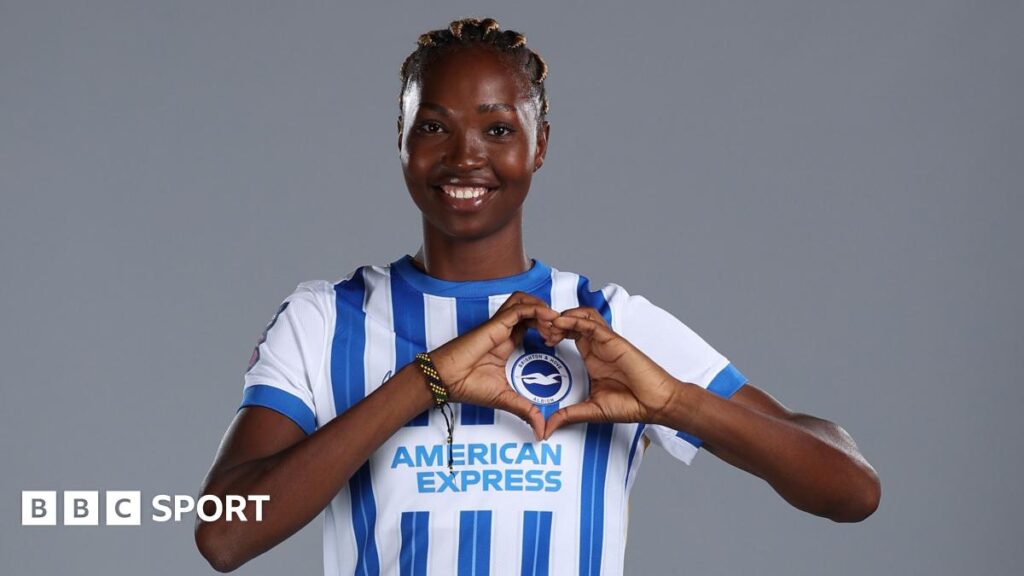 Aisha Masaka with hair tied up and wearing a bright pink Brighton top trains along with team-mates who can be seen in the background